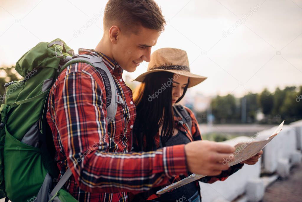 Hikers with backpacks looks on map, excursion in tourist town. Summer hiking. Hike adventure of young man and woman