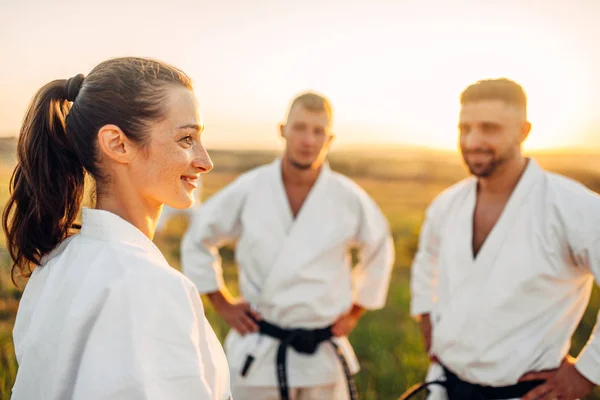 Two male and one female karate fighters on training in summer field. Martial art workout outdoor, technique practice