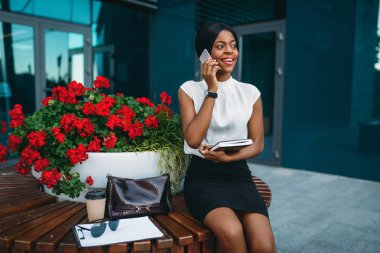 Cep telefonuyla konuşurken siyah iş kadını ve o zaman saati ofis binası önünde görünüyor. İşkadını etek ve beyaz bluz, müzakere açık havada gülümseyen