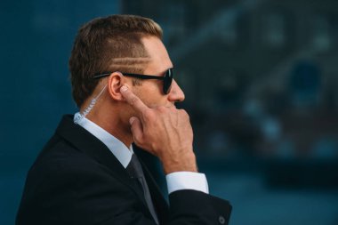 Erkek koruma kulaklık tarafından açık havada, güvenlik iletişim araçları konuşuyor. Profesyonel koruma riskli bir meslektir. Takım elbise ve güneş gözlüğü korumak