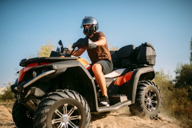 Kask içinde atv binici ile ormandaki kumlu yolda gidiyor. Quad bisiklet, aşırı spor sürme ve seyahat, quadbike macera