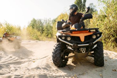 Kask içinde iki atv bisikletçi kum, offroad ormandaki bir daire içinde binmek. Quad bisiklet, aşırı spor sürme ve seyahat, quadbike yaz macera
