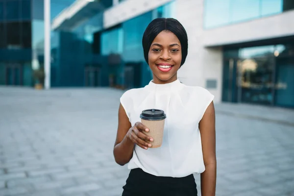 屋外での段ボールのコーヒー カップ 背景にビルを持つ女性実業家を笑っています スカートと白のブラウスに黒の実業家 — ストック写真