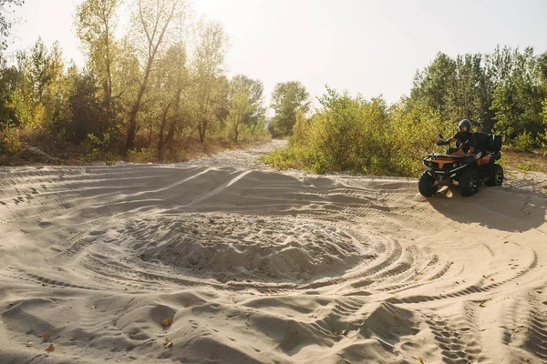 森の背景に太陽の光で Atv ライダー ヘルメット登山で砂浜道路 オフロード エクストリーム スポーツ クワッド バイクに乗って Quadbike — ストック写真