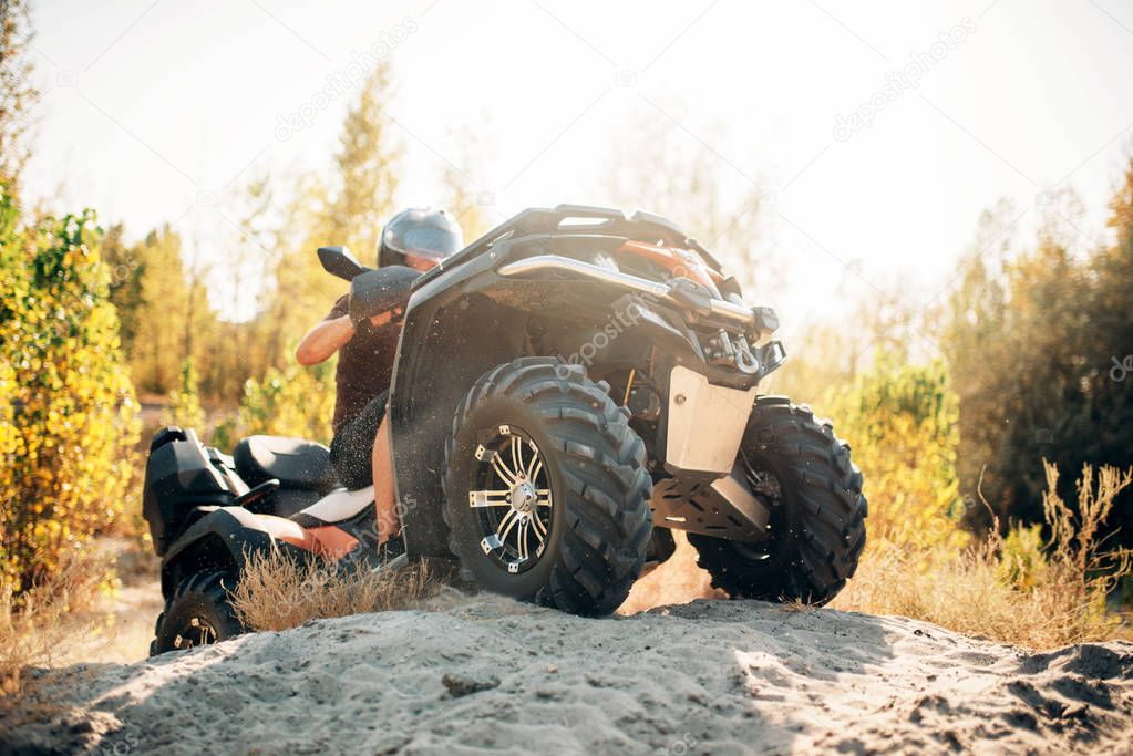 Atv rider climbing the sand mountain in quarry. Male driver in helmet on quad bike in sandpit