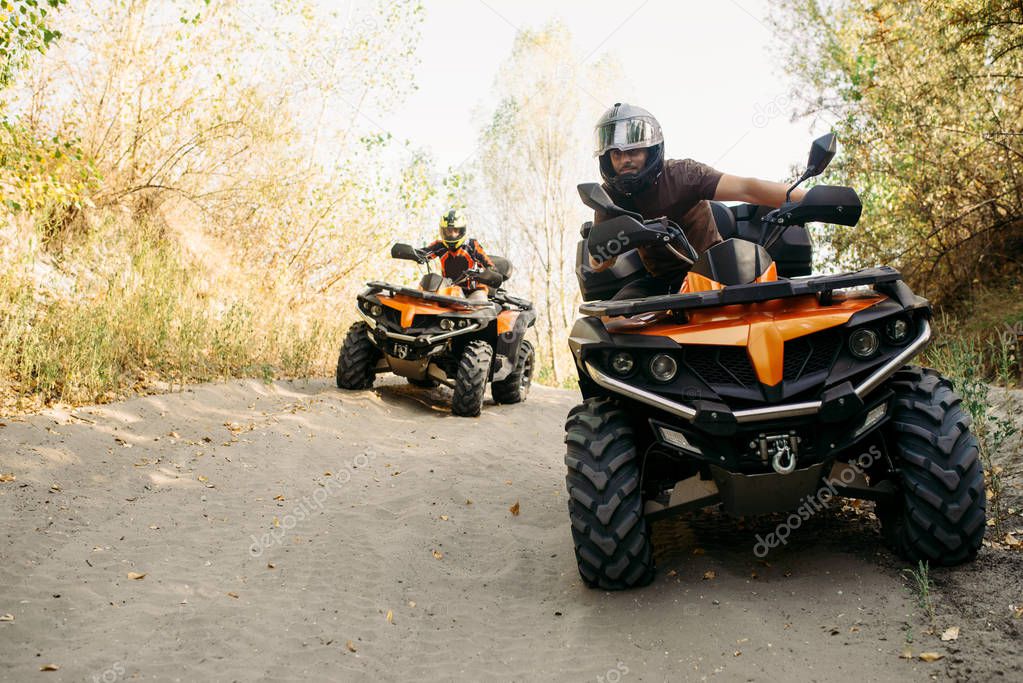 Two quad bike riders in helmets travels in forest, front view. Riding on atv, extreme sport and travelling, quadbike adventure