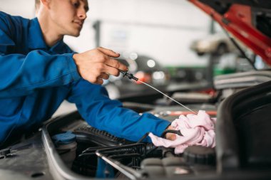 Erkek teknisyen araba motor yağ seviyesi yağ çubuğu ile denetler. Otomatik-servis, araç bakım, tamirci araçları ile