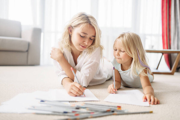 Mother and daughter draw with pencils lying on the floor. Parent feeling, togetherness
