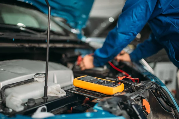 Car electrician with multimeter checks the battery level. Auto-service, vehicle wiring diagnostic
