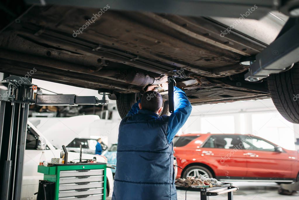 Repairman with a wrench checks the suspension, car on the lift. Automobile service, vehicle maintenance
