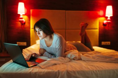 Mutlu kadın yalan yatak ve uses laptop, Günaydın, yatak odası interoir arka plan üzerinde. Bayan uyanma