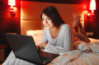 Yatakta yatan ve dizüstü bilgisayar ekranında, Günaydın, yatak odası interoir arka plan üzerinde seyir kadın. Bayan uyanık
