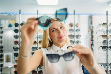 Kadın alıcı güneş gözlükleri optik mağaza, vitrin arka plan üzerine gözlük ile seçer. Seçimi gözlük dükkanı, optometri kavramı gözleri koruma