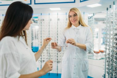 Kadın gözlükçü gözlük optik mağaza alıcıya gösterir. Gözlük seçimi ile profesyonel göz doktoru