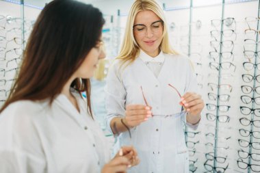 Kadın gözlükçü gözlük optik mağaza müşteri için gösterir. Gözlük seçimi ile profesyonel göz doktoru