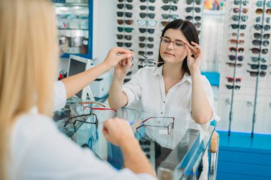 Kadın gözlükçü ve tüketici optik mağazada gözlük çerçeve seçer. Gözlük seçimi ile profesyonel göz doktoru