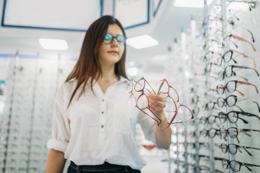 Genç kadın alıcı birçok gözlük el, optik mağaza, vitrin arka plan üzerine gözlük ile tutar. Gözlük dükkanı kavram, gözlük seçim profesyonel eyecare