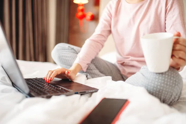 在睡衣的女性人喝咖啡 并在床上使用笔记本电脑 早上好 卧室界面的背景 — 图库照片