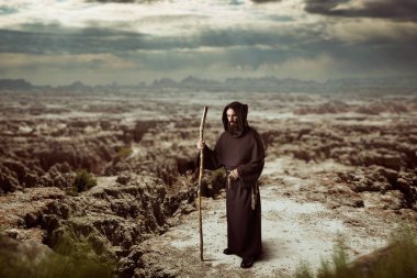 Medieval monk in black robe with hood is walking in the desert clipart
