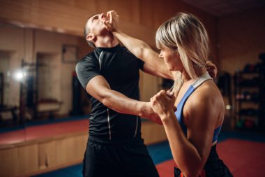Kadın kişi kendini savunma egzersiz erkek kişisel antrenör ile spor salonu iç arka plan üzerinde. Kadın yapar yumruk boğaz eğitim için kendini pratik savunma