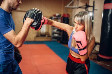 Egzersiz ile yastıkları erkek kişisel antrenör, spor salonu iç arka plan üzerinde üzerinde kadın kick boks şampiyonu. Eğitim, kickboks pratik yumruk el kadın boksör yapar