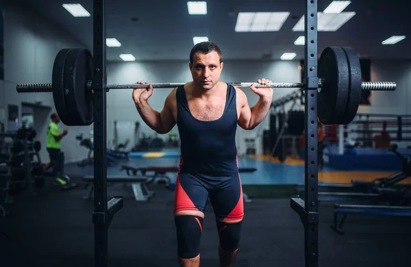 Muscular athlete in sportswear poses at the stand with barbell in gym. Weightlifting workout, lifting