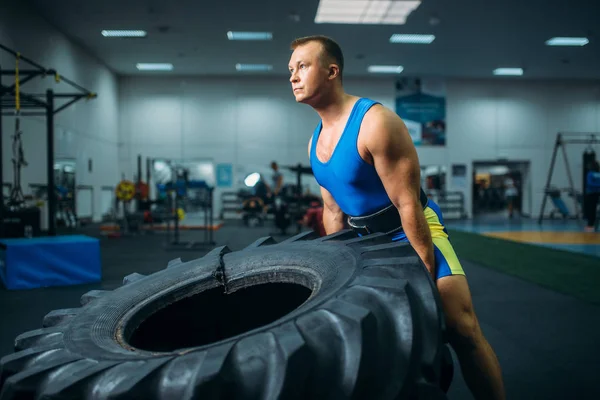 Strong male athlete doing strength exercise with truck tyre in gym, crossfit workout. Cross fit training in sport club