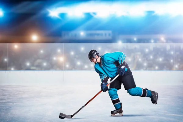 One hockey player on ice in action, arena spotlights and tribunes with fans on background. Male person in helmet, gloves and uniform holds stick in hands