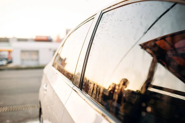 Car glass with drops of wax closeup, side view, nobody. Touchless self-service car wash outdoor. Automobile washing. Vehicle cleaning at summer day