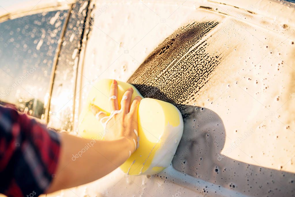 Female person hand with sponge scrubbing vehicle with foam, car wash. Young woman on self-service automobile washing. Outdoor carwash