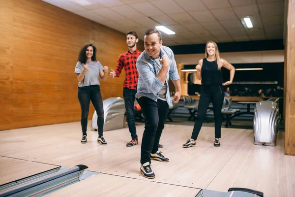 Male bowler throws ball on lane, strike shot. Bowling alley teams playing the game in club, active leisure