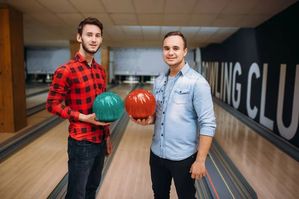 Two male bowlers poses on lane with balls on hands. Bowling alley players before competition. Classical tenpin game in club, active leisure
