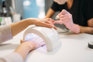 Kadın müşteri jel vernik çivi kurutma makinesi, Relax arka plan, güzellik salonları üzerinde pembe eldiven içinde kurur. Manikürcü El Bakımı kozmetik prosedür yapıyor