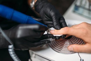 Siyah eldiven kadın ana salonda manikür bir adam yapar. Manikürcü tırnak parlatma yapıyor