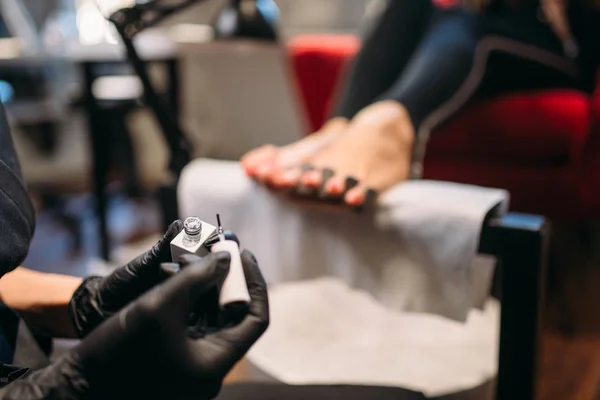 修脚大师在黑色手套油漆与清漆脚指甲的女性客户 美容院 专业指甲护理 — 图库照片