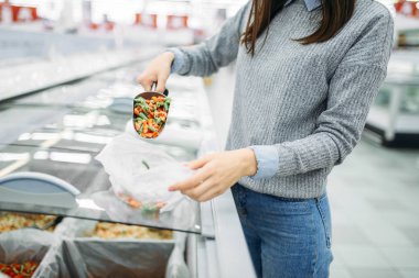 Kadın bir süpermarkette dondurulmuş sebzeler bir paket alır aile alışveriş. Kadın müşteri salonu, alıcı pazarında ürünleri satın alır.