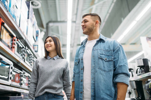 Пара, которая смотрит на полку с электрическими печами в супермаркете. Клиенты в магазине, семья выбирает товары народного потребления
