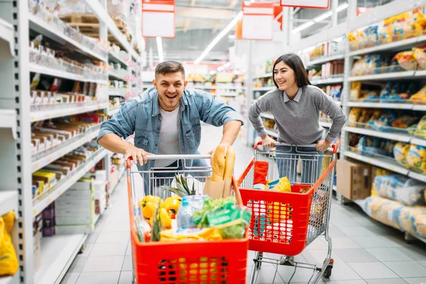 Oynak çift binmek arabaları üzerinde süpermarkette, aile alışveriş. Müşteriler alıcılar pazarında eşya,
