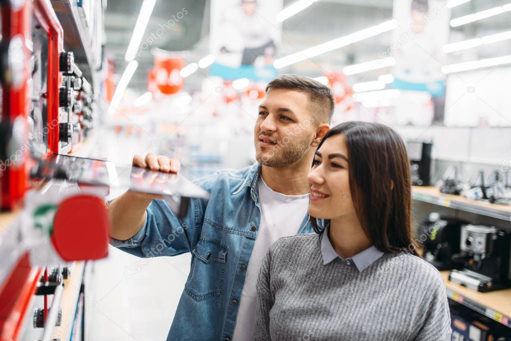 Couple buys an electric oven in a supermarket. Customers in shop, family choosing consumer goods