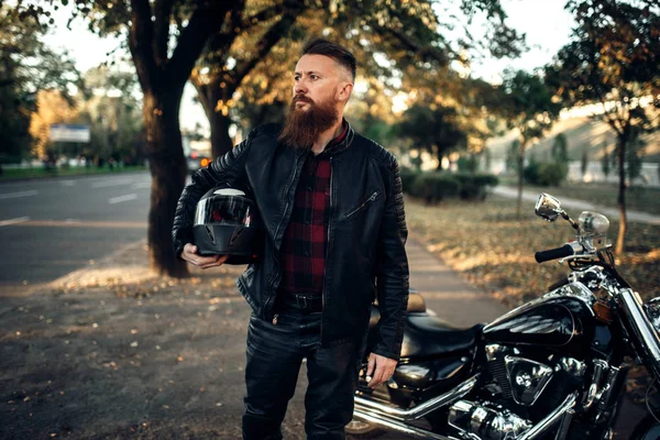 Biker in leather jacket standing near black chopper. Vintage bike, rider and his motorcycle