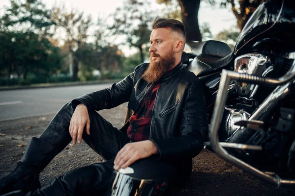 Biker in leather jacket relax after road travel on his chopper. Vintage bike, rider and his motorcycle, freedom lifestyle, biking