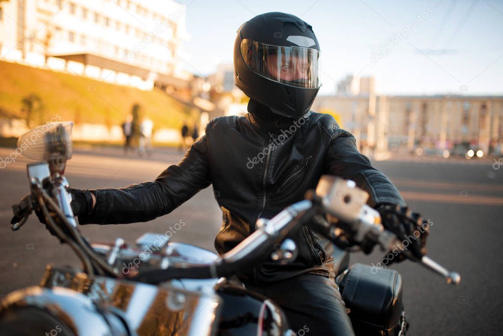 Biker in leather jacket and helmet with visor sitting on classical chopper. Vintage bike, rider on motorcycle