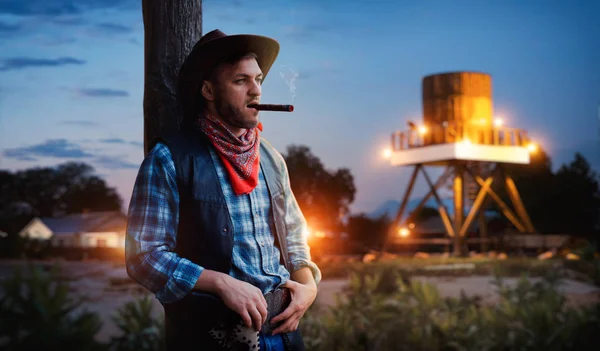 残酷的牛仔在日落时抽雪茄 晚上在西部的德州牧场放松一下 老式男性与枪在农场 狂放的西部文化 — 图库照片