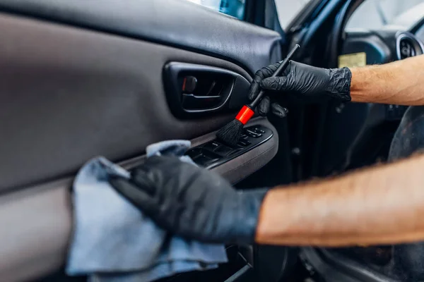 Auto detailing of car interior on carwash service. Worker in gloves cleans door trim with brush