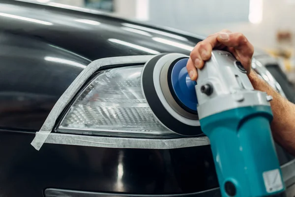 Auto detailing of car headlights on carwash service. Worker cleaning glass with polishing machine