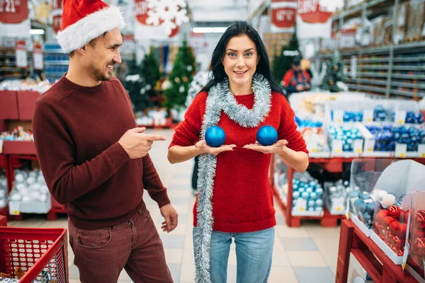 有趣的夫妇选择装饰在商店和笑话 女人把圣诞球在她的胸前 12月假日物品的购物 — 图库照片