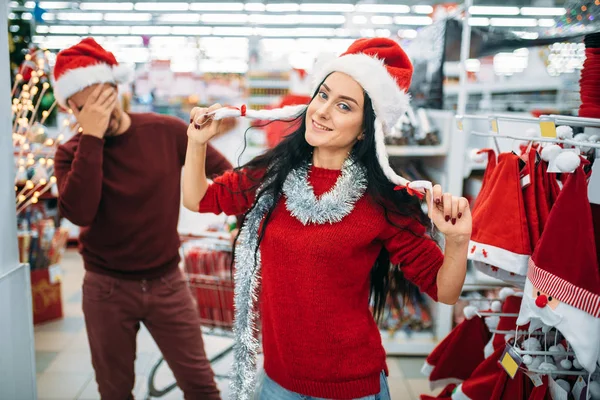 Funny young couple trying on christmas clothes in supermarket, family tradition. December shopping of holiday goods and decorations