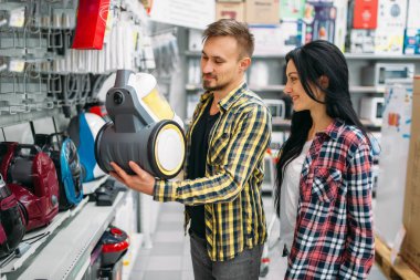 Genç seçerek elektrikli süpürge süpermarkette çift. Kadın ve erkek müşteriler aile alışveriş üzerinde. Erkek ve kadın ev için mal satın alma