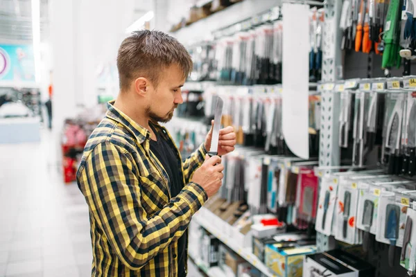 Young man buying kitchen knife in supermarket. Male customer on  shopping in hypermarket, department of products for the kitchen