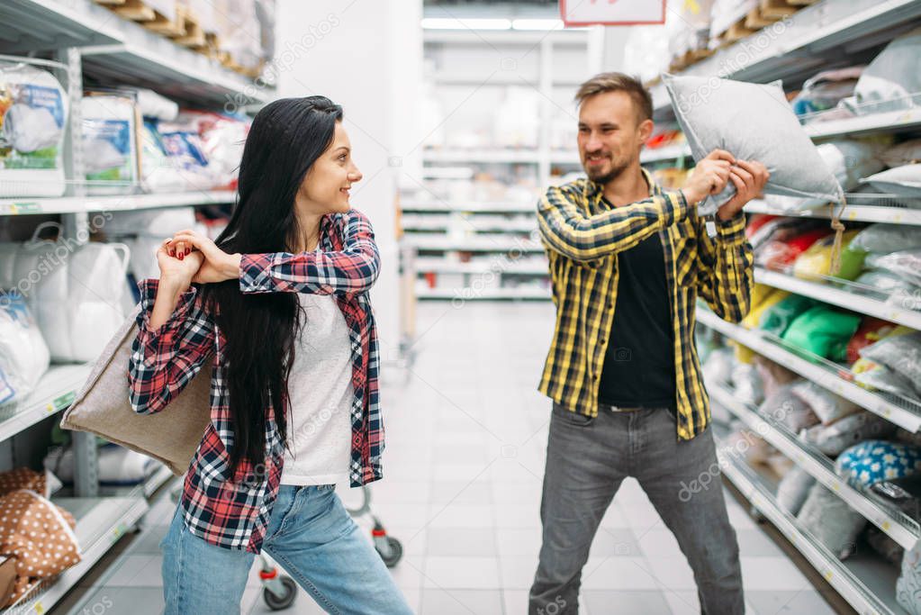 Playful couple in supermarket, pillow fight. Male and female customers on family shopping. Man and woman purchasing goods for the house